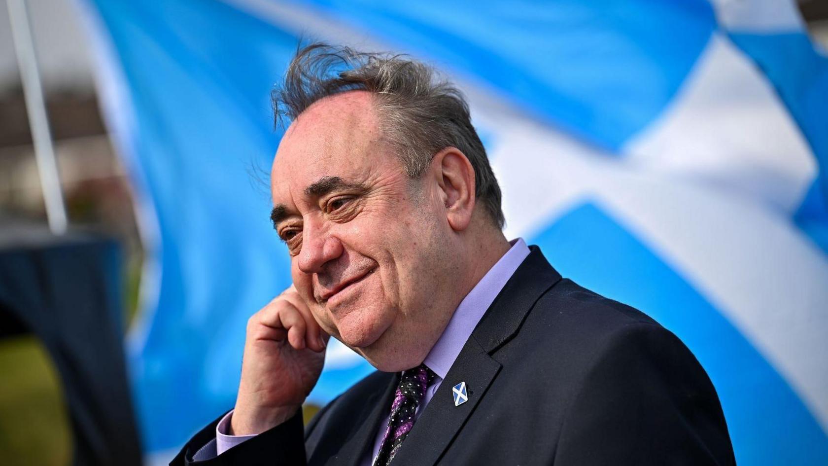 A grinning Alex Salmond, with his hand to his ear and a saltire flag in the background