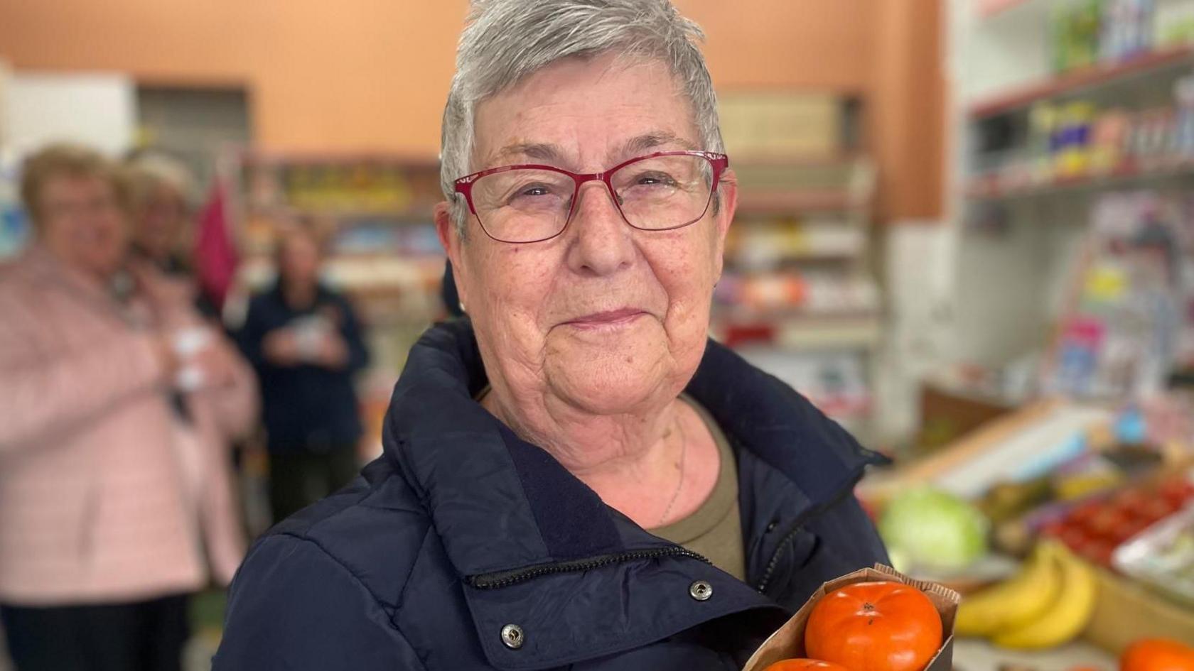 A middle aged woman smiles holding up some orange fruit.