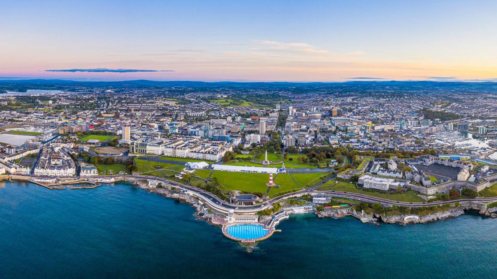 An aerial shot of Plymouth city centre showing the Tinside Lido and Smeaton's Tower in the foreground and views out to Dartmoor in the distance.