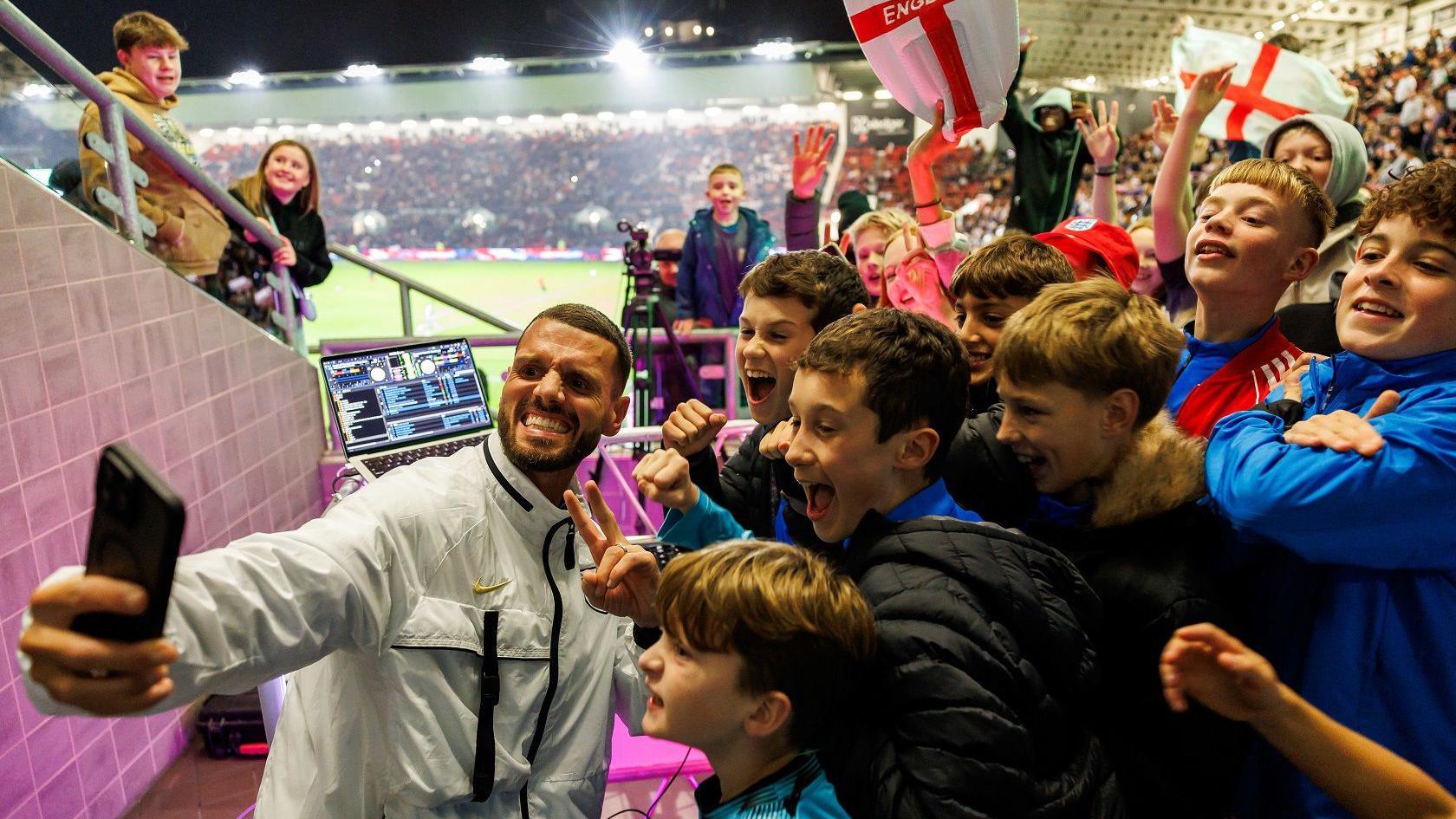 Dozens of young football fans pose for the camera as a man takes a selfie during the England Under-21 match at Ashton Gate Stadium