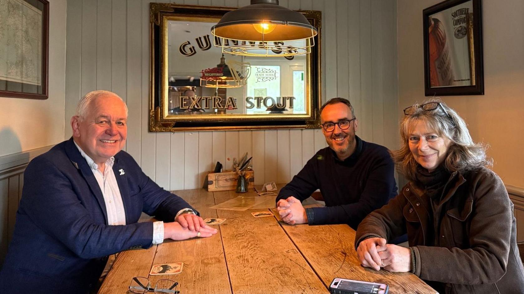 Former police officer, John Daniels, wears a blue jacket and white shirt and local, Sue Warner, wears a brown coat and they are pictured around a pub table with reporter, Matt Murray.