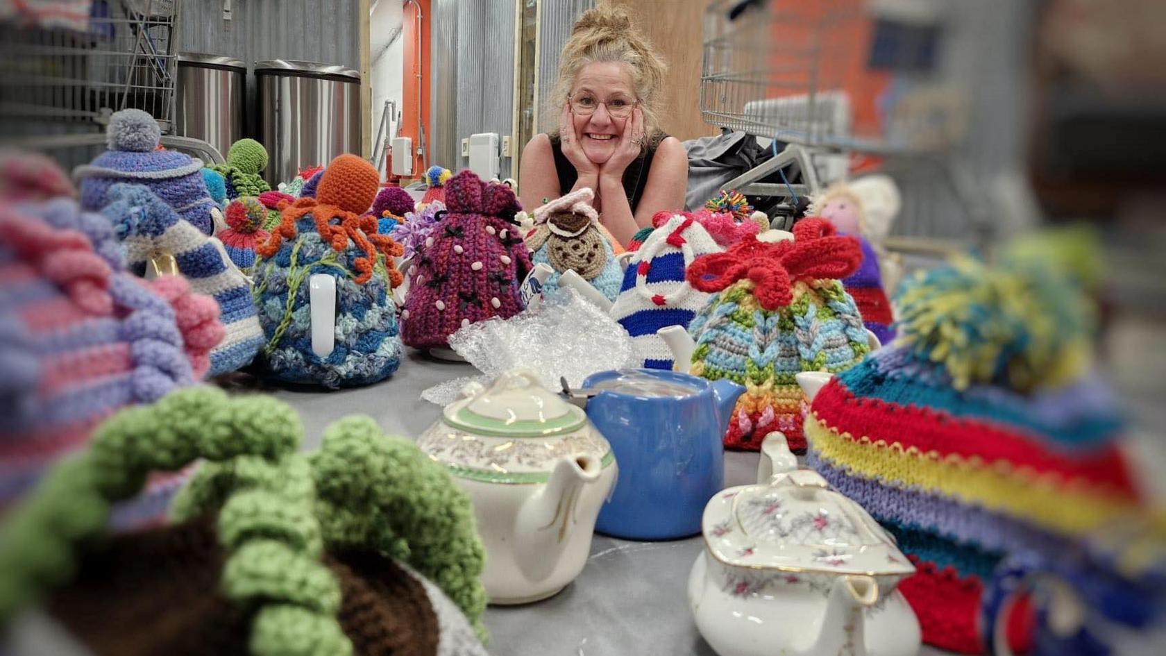 A lady looking at lots of tea cosies displayed on teapots