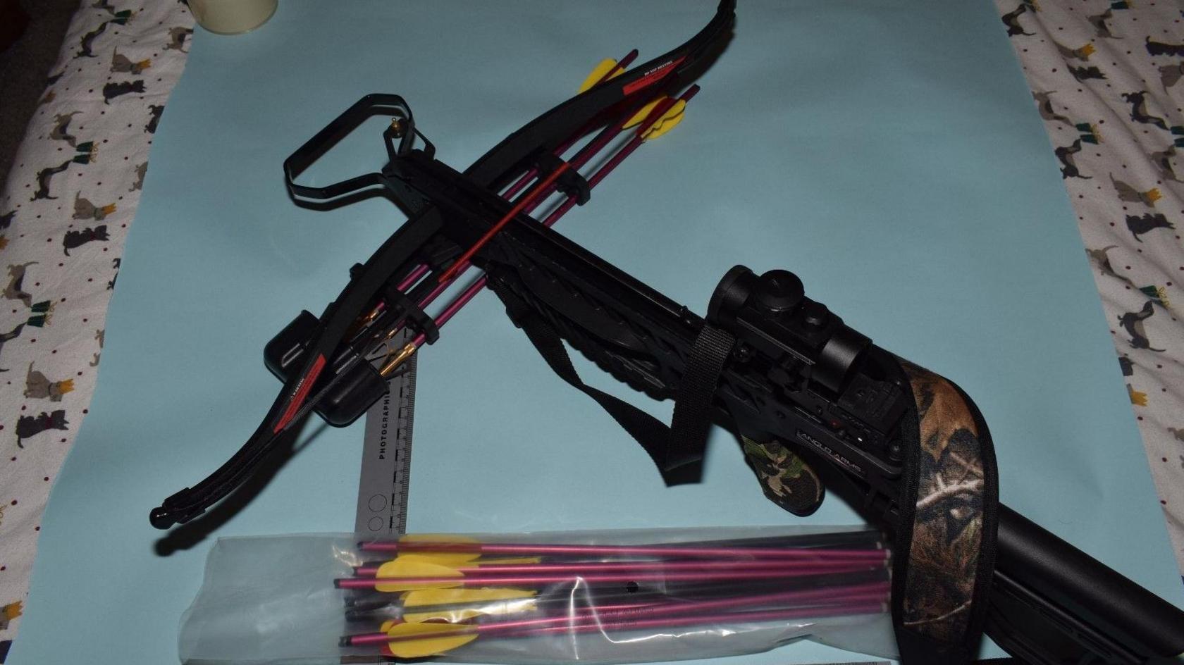 A crossbow with arrows in a packet, lying on a light-coloured sheet.