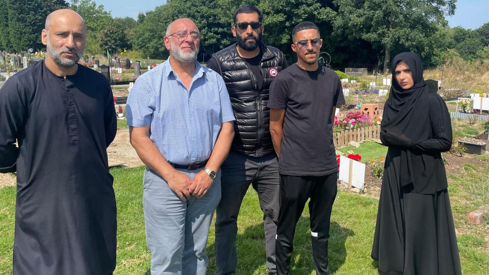 Muslim adults dressed in black standing in a cemetery