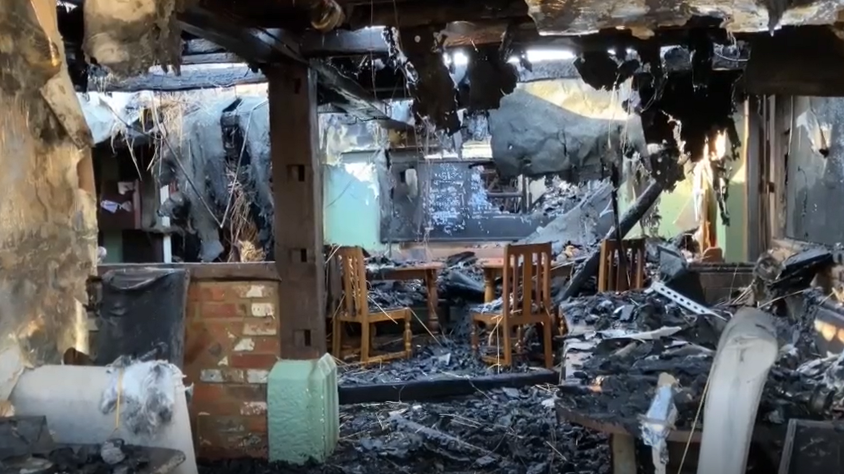 A fire-damaged building with burned timbers and wooden chairs.