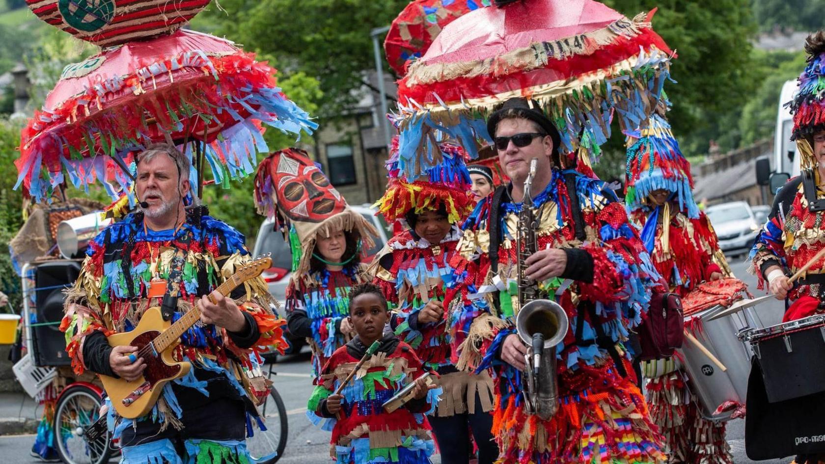 A group in the carnival procession with instruments and colourful costumes, made up of strips of material.