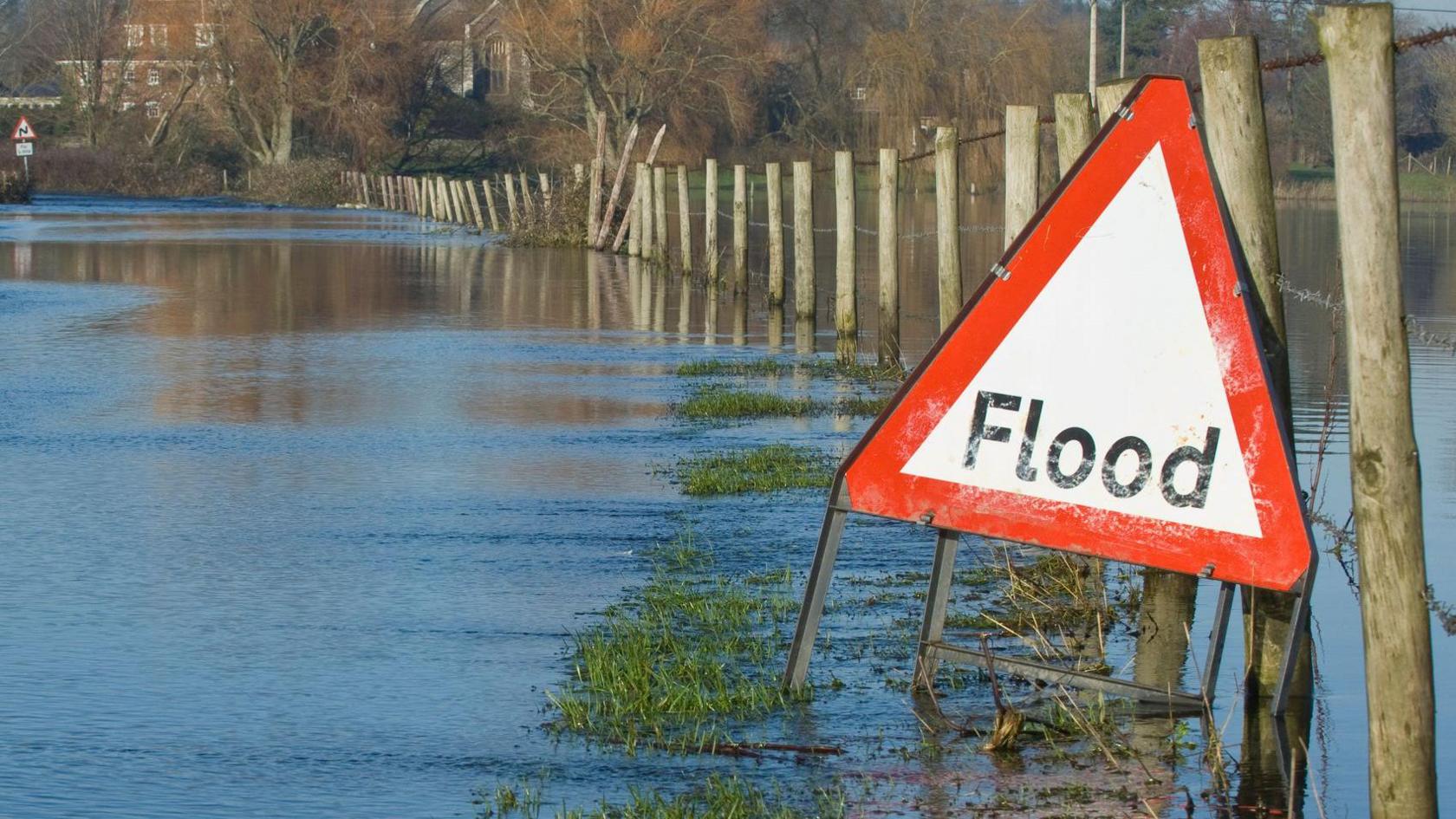 A stock image of a flooded field with a triangular "flood" warning sign.