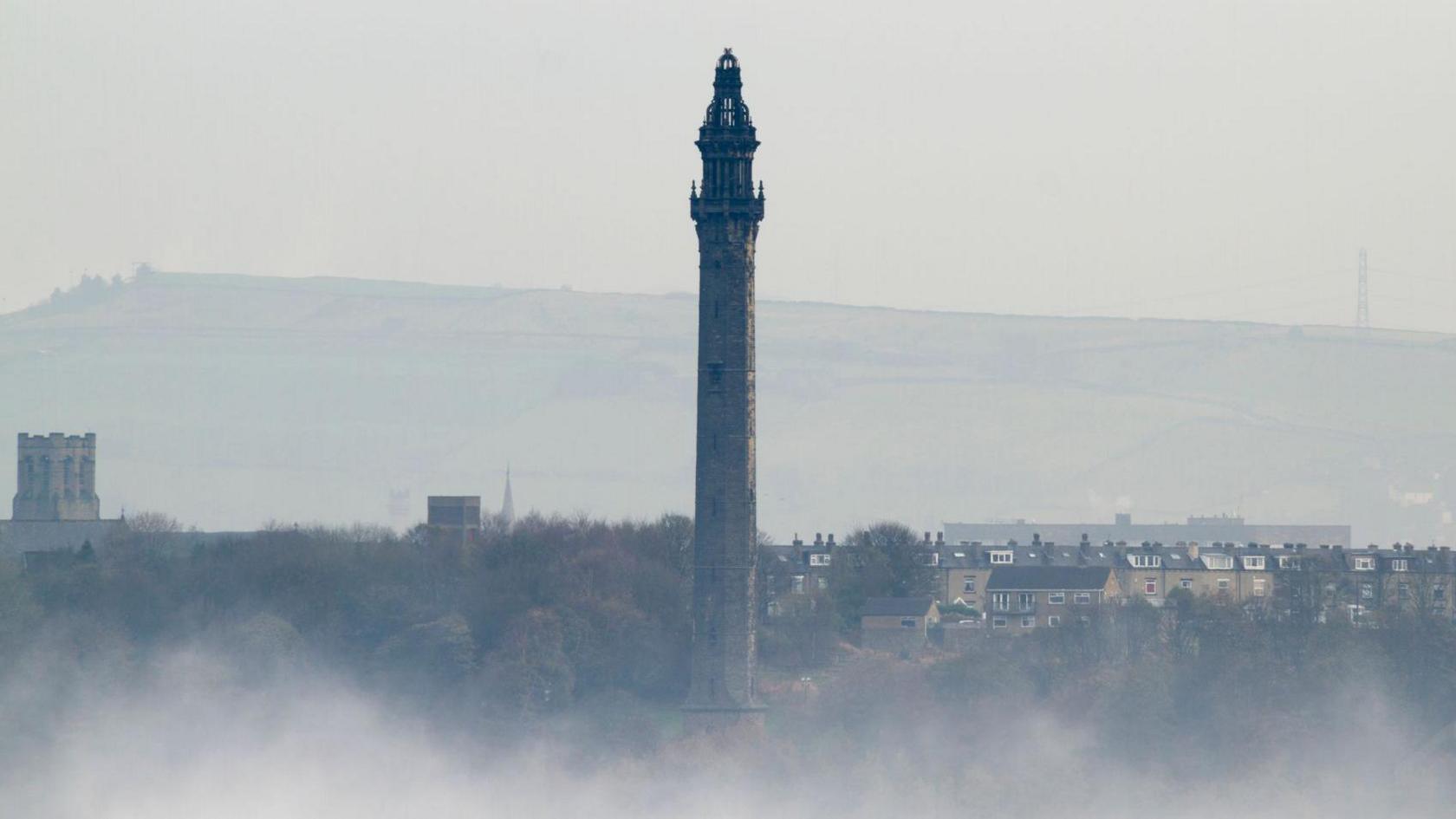 A gothic-looking tower rises above a town at twilight with moorland in the background
