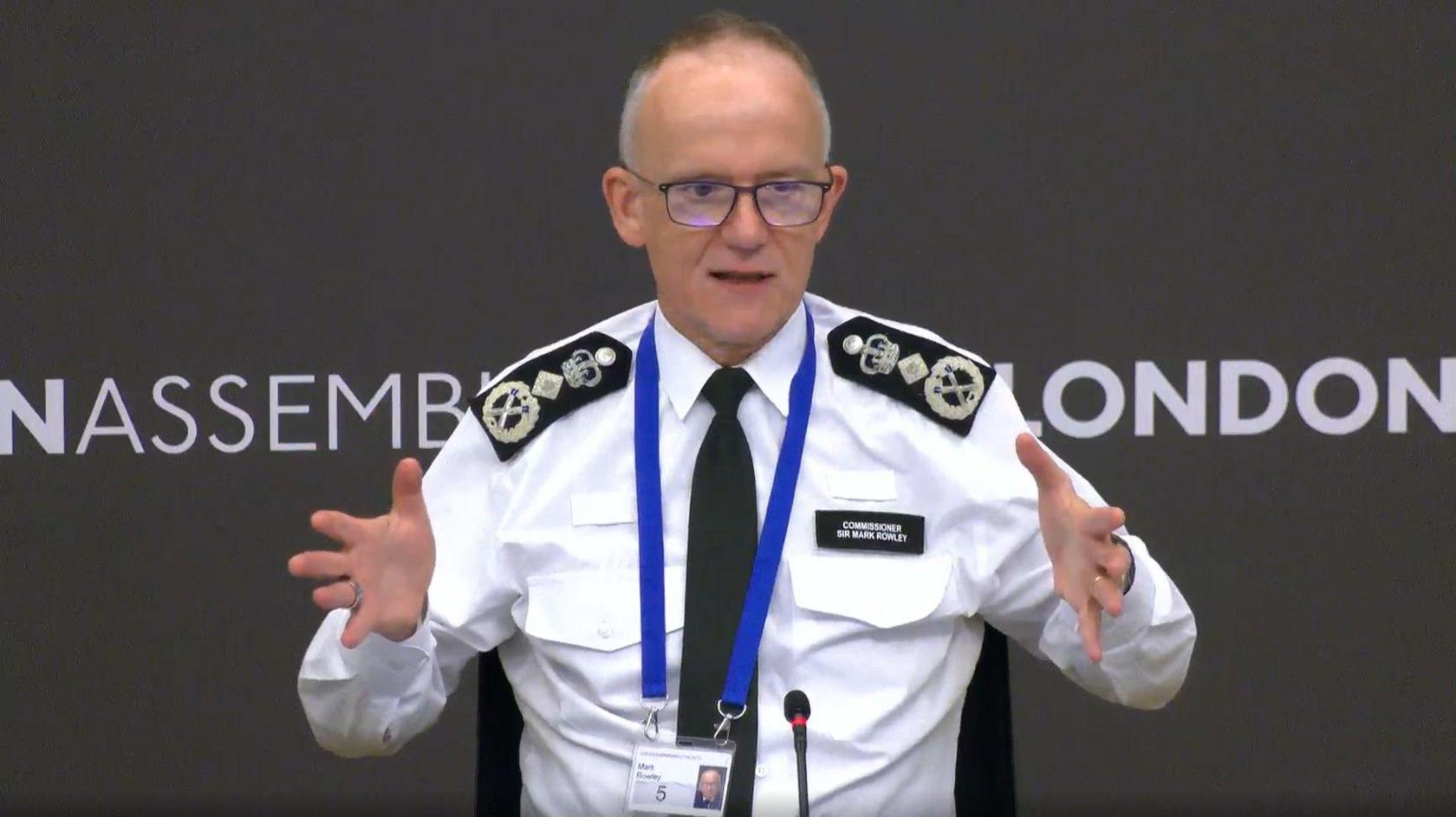 Sir Mark Rowley addresses the Police and Crime Committee. He is wearing a white shirt with a black tie and there is a lanyard around his neck.