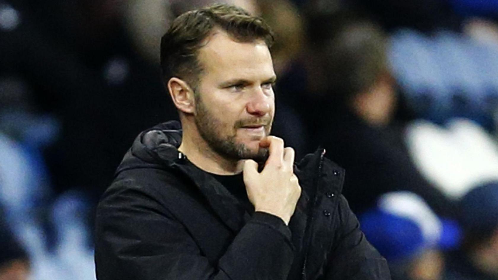 Tom Cleverley scratches his chin while standing on the touchline