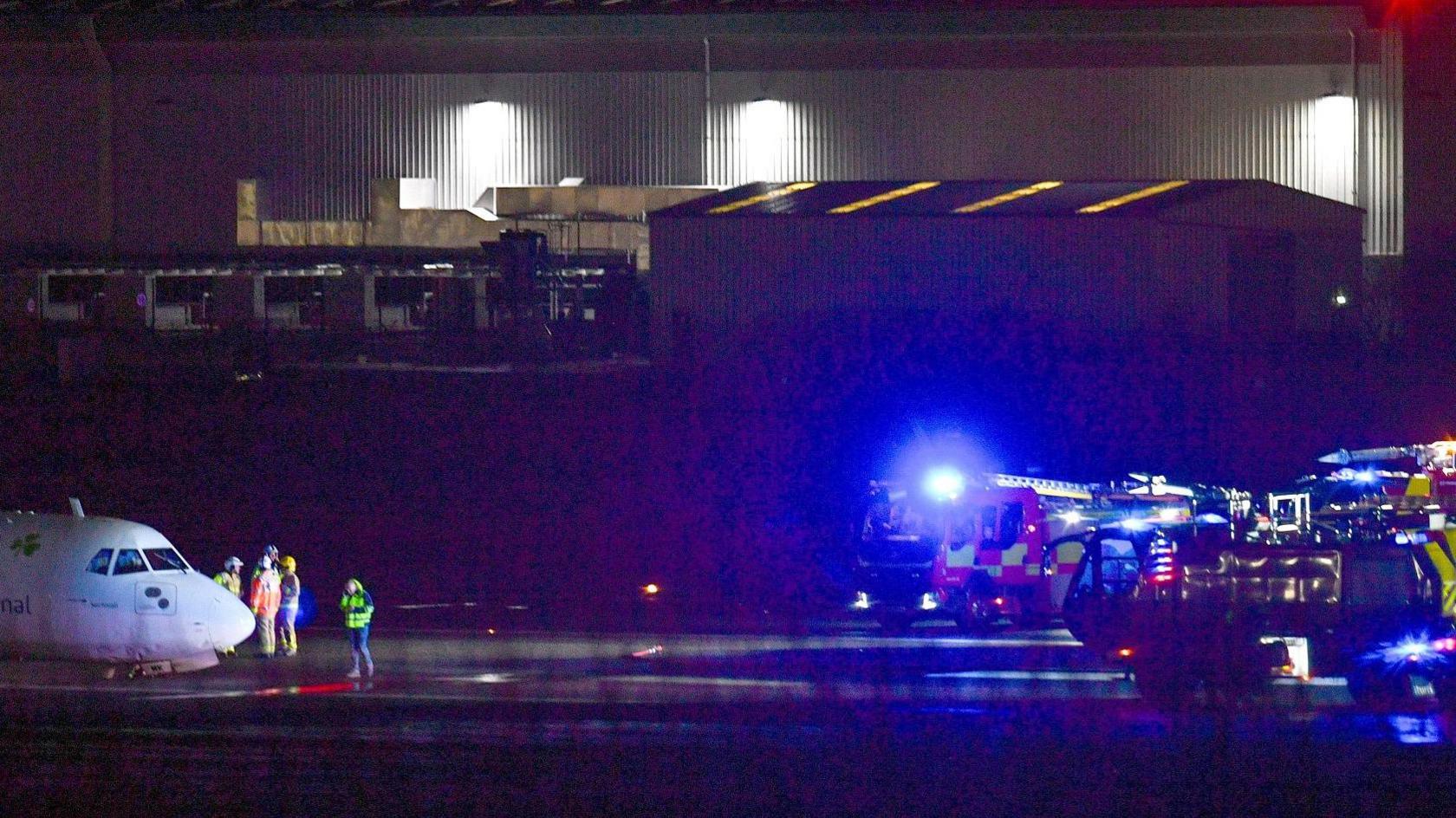 Fire crews on the runway at Belfast City Airport, parked in front of an Aer Lingus plane which suffered a hard landing.  A number of emergency workers are standing next to the plane. 