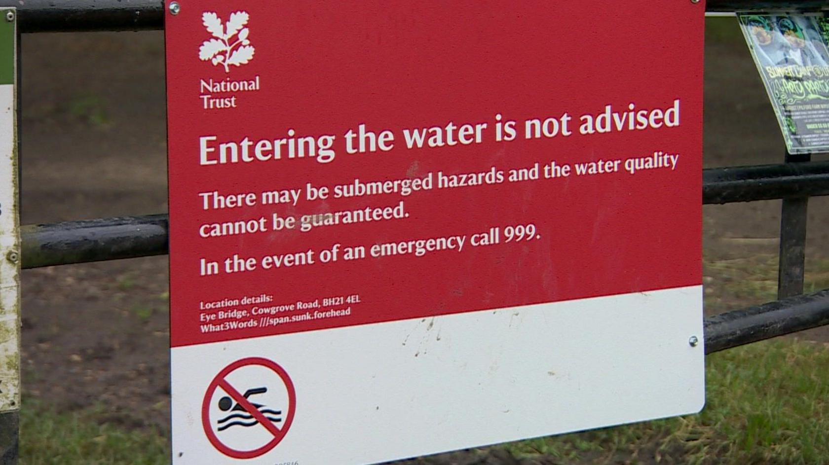 A red National Trust sign says entering the water is not advised and the water quality cannot be guaranteed