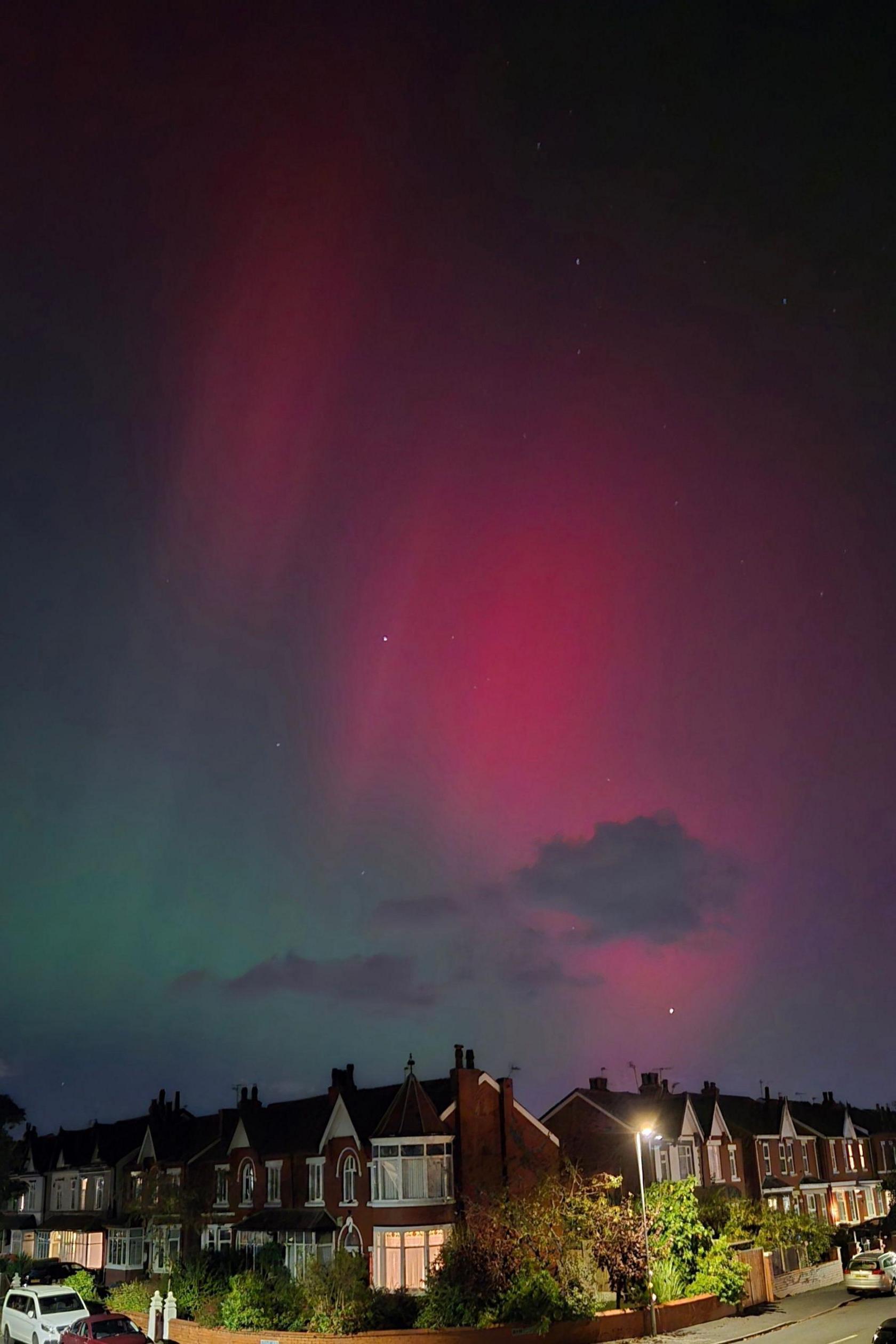 A darker sky is also split in dark green and purple-pink above a street of houses in Southport