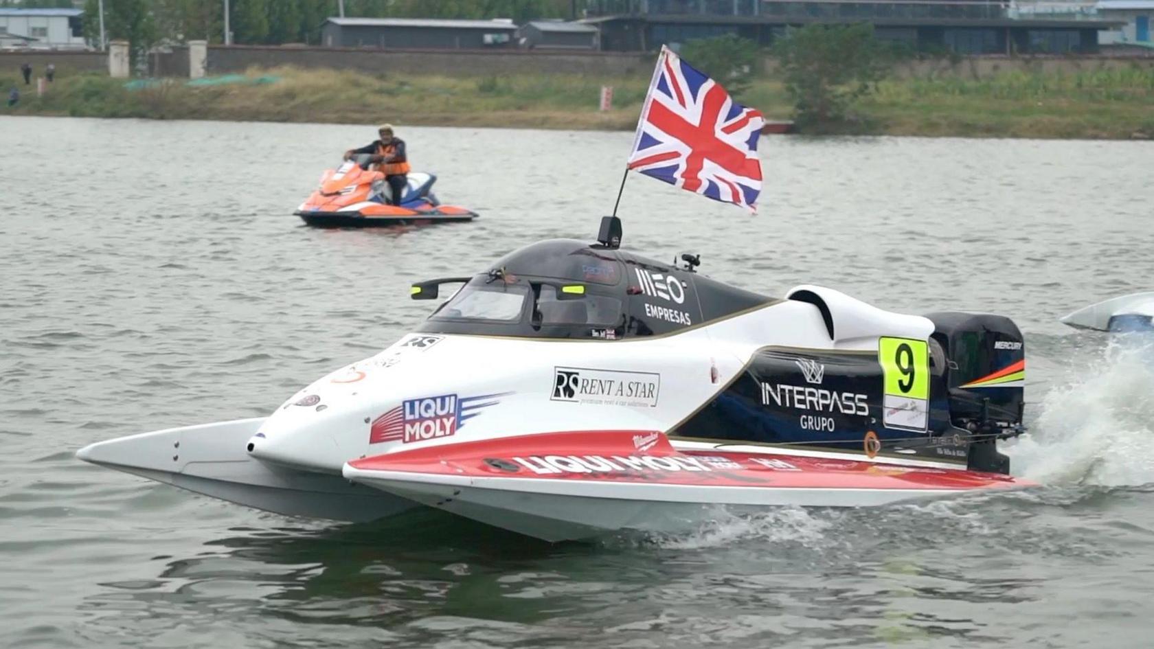 A red and white powerboat on grey water. The boat has a Union Jack on the top