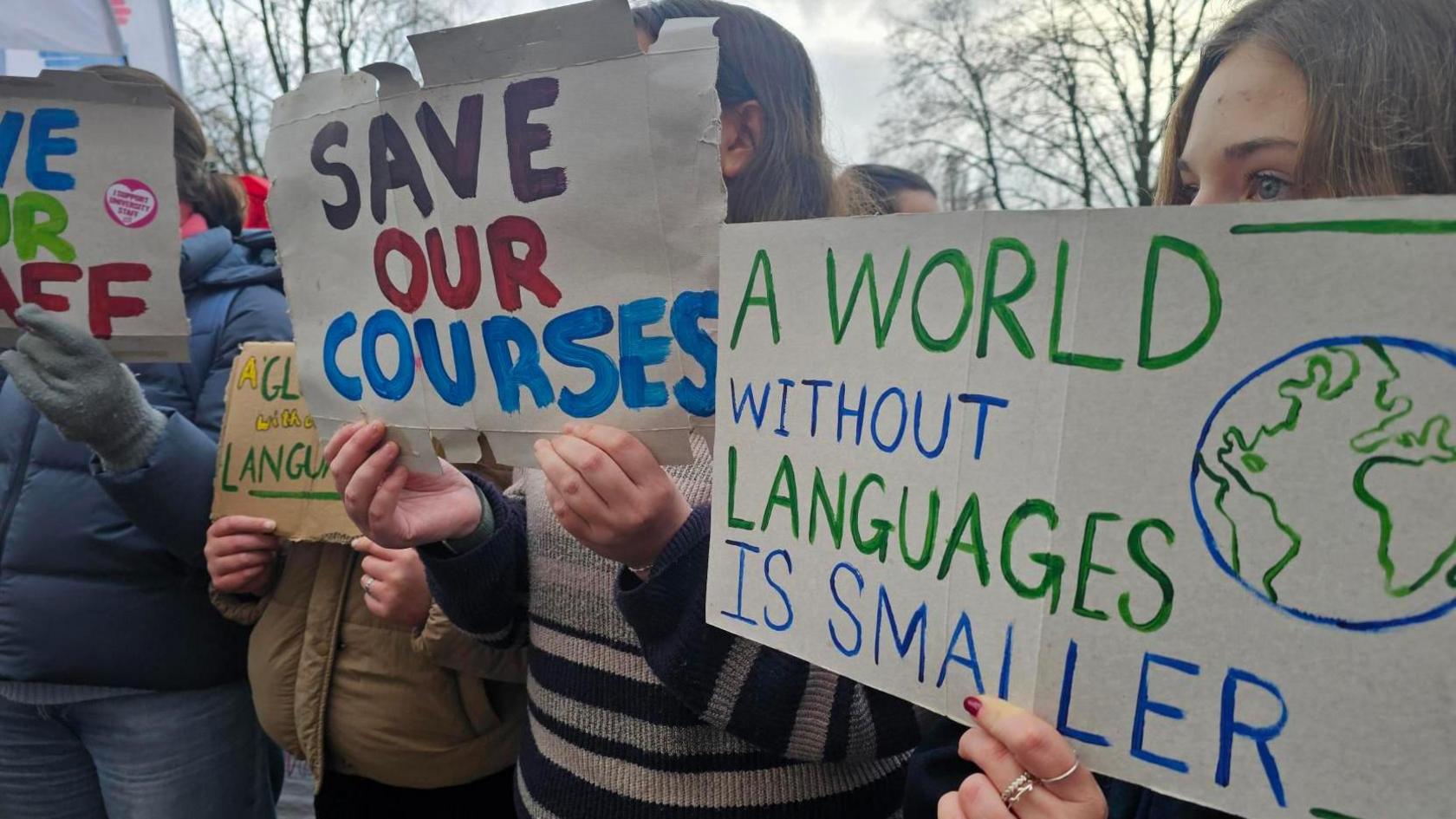 People holding up homemade placards which say "save our courses" and "a world without languages is smaller"