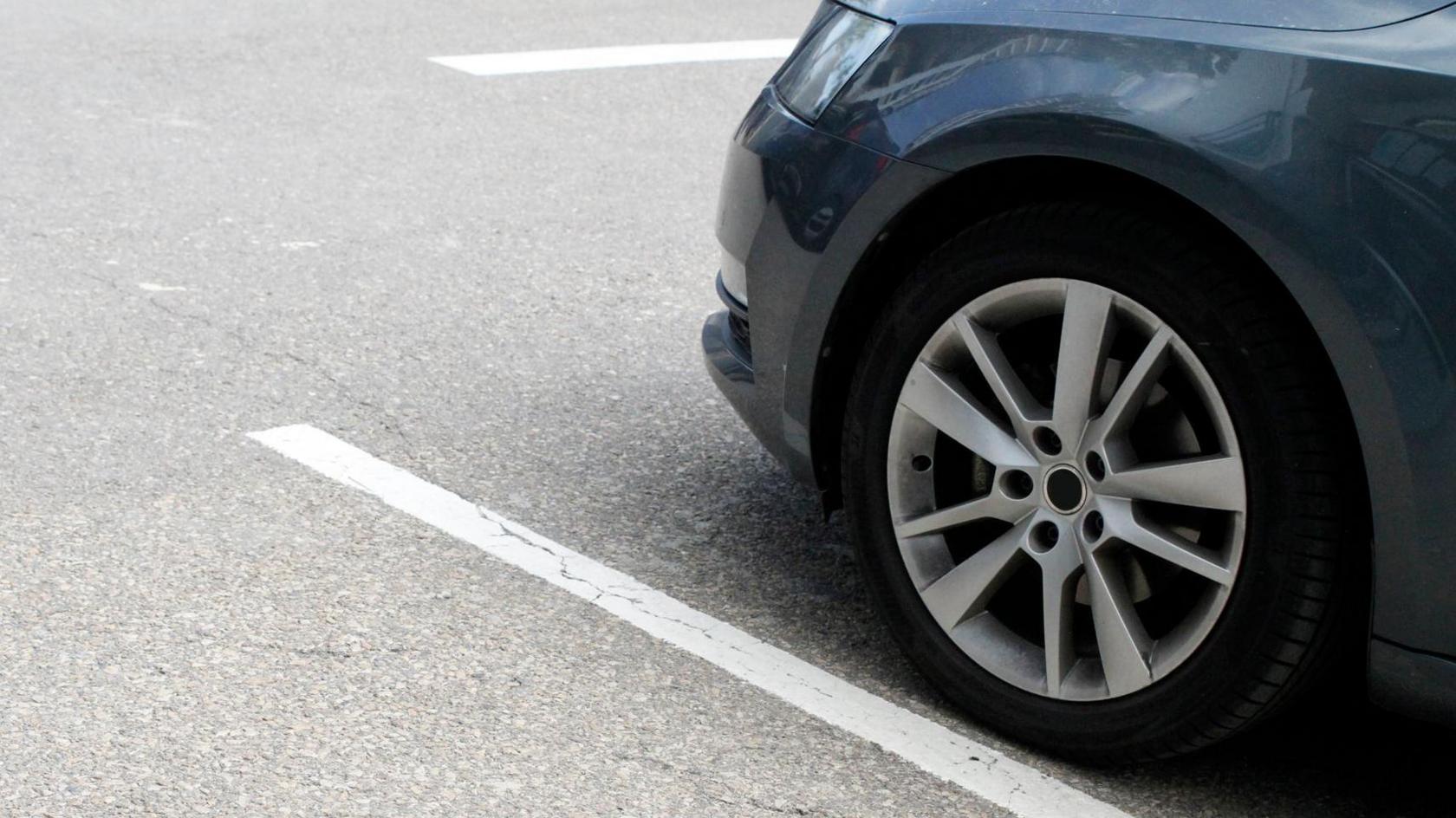 A lower portion of a blue car is parked next to a white line in a car park.