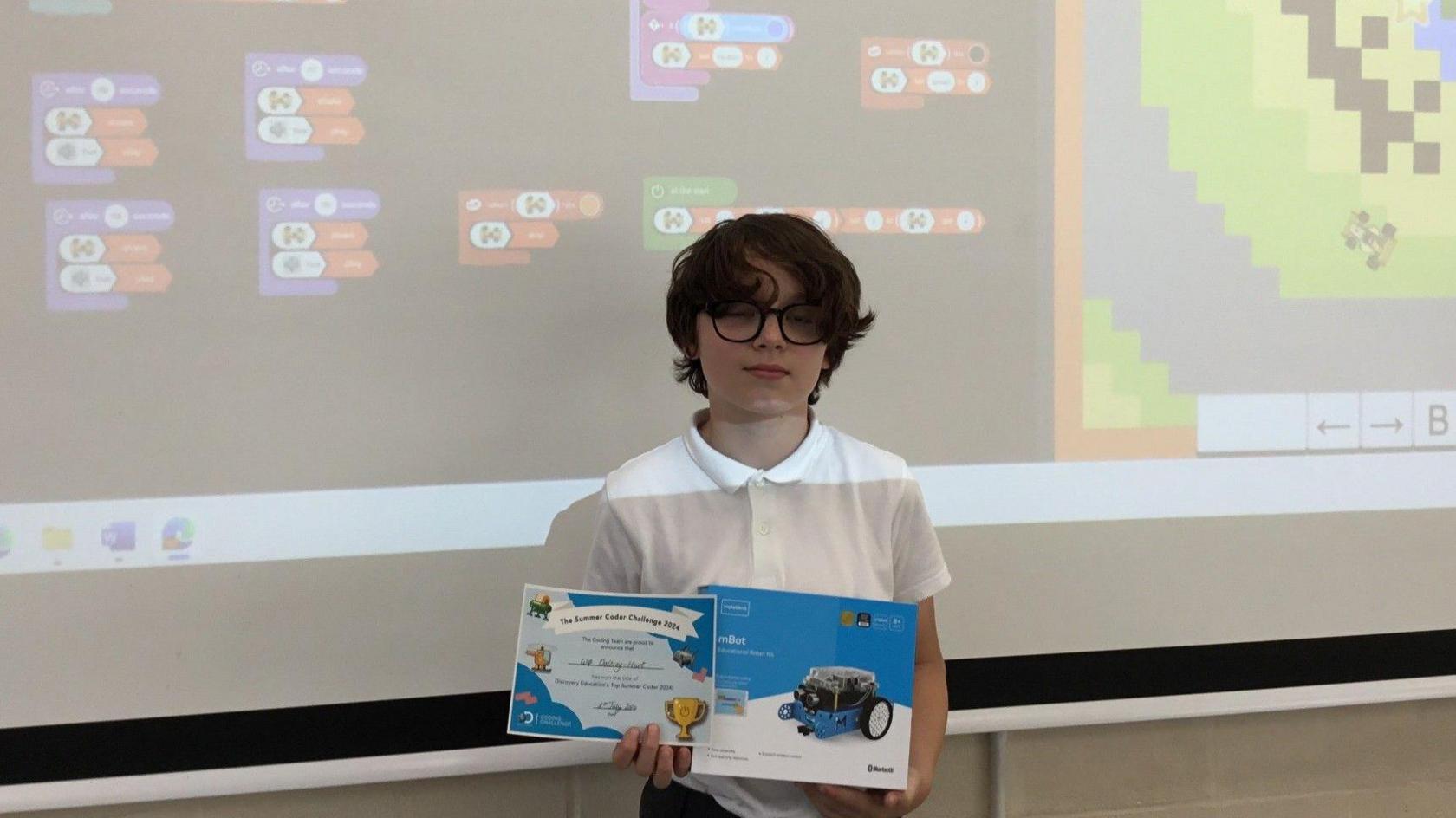 Wilf looks into the camera holding up his certificate with game on the interactive whiteboard behind him