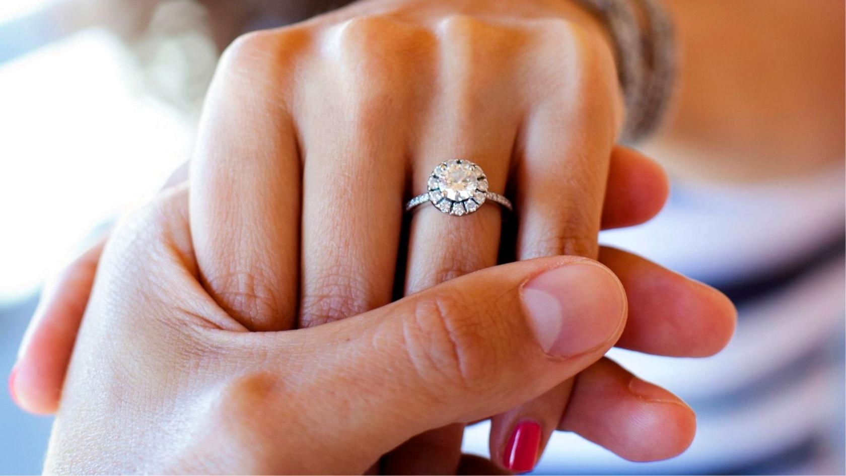 A close up of a man holding a woman's hand with a diamond engagement ring