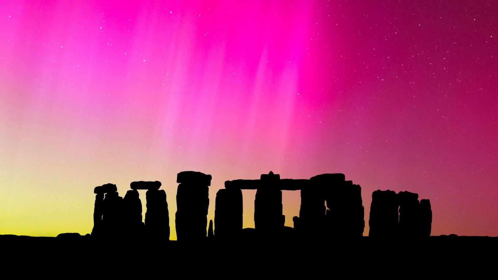 Stonehenge stones are silhouetted against a bright pink and slightly yellow sky.