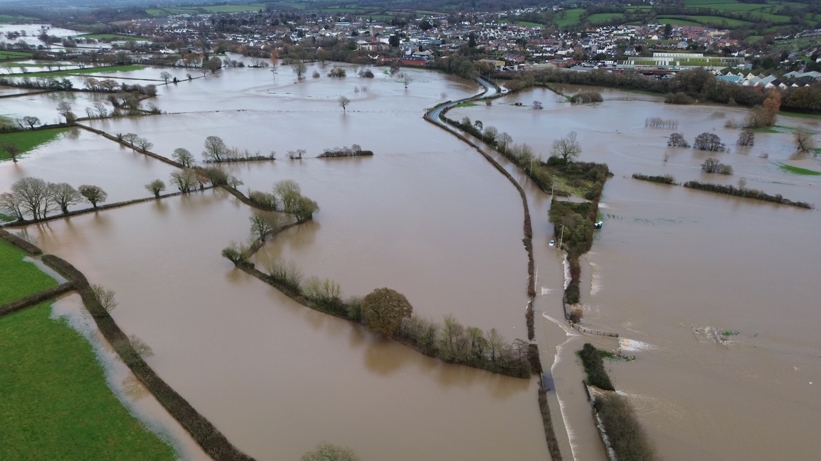 Drone images of flooding at Axminster, Devon - town in the distance with fields and roads flooded with brown water