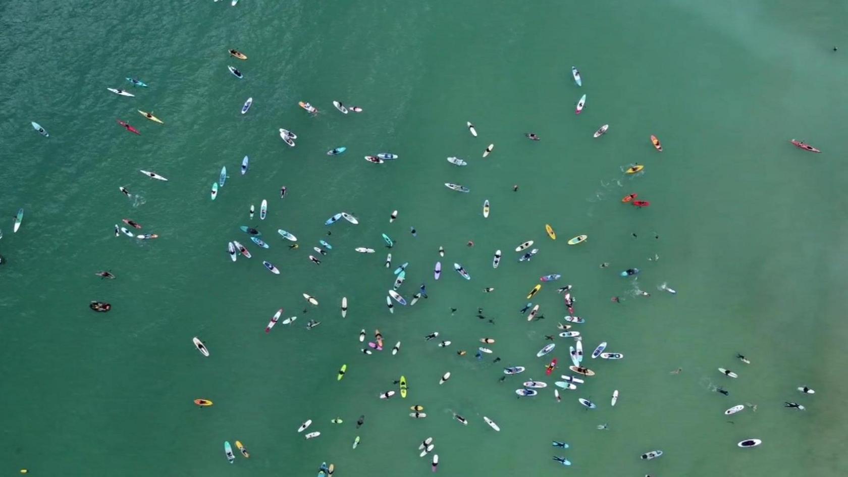 A drone shot of lots of swimmers and surfers in the water at Gylly beach. The sea looks a greenish blue.