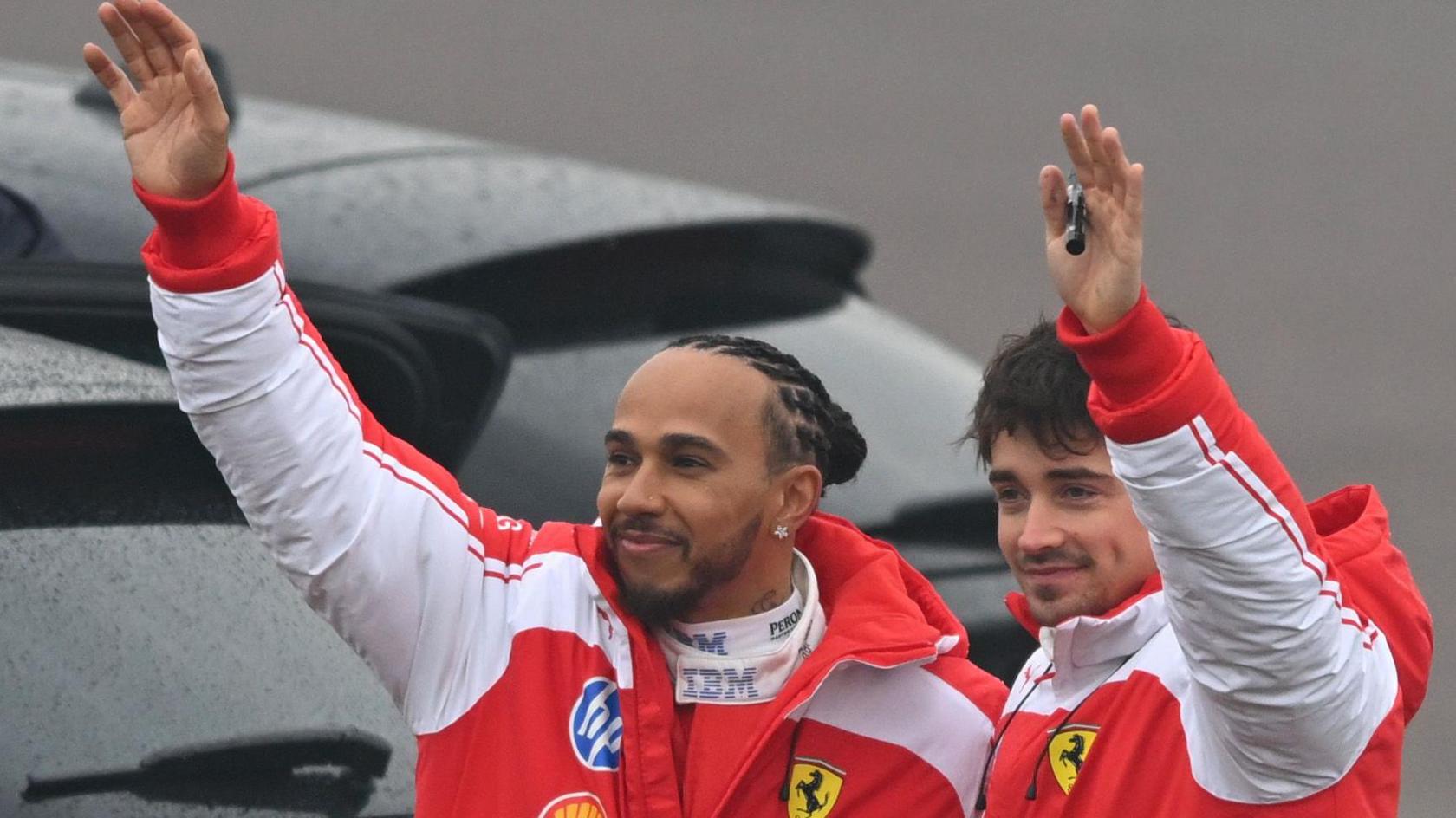 Lewis Hamilton and Charles Leclerc, both wearing Ferrari jackets, waving at fans gathered outside the Fiorano circuit in Italy