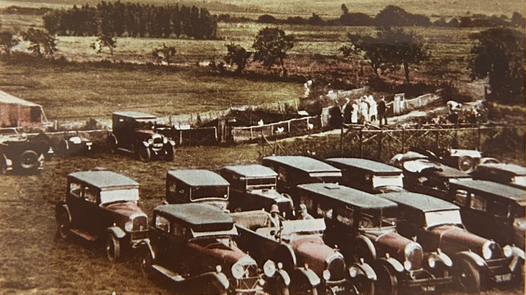 A black and white image of classic cars parked at Drusillas. The photo, dated to the 1920s, shows 12 cars parked in two rows in a field.