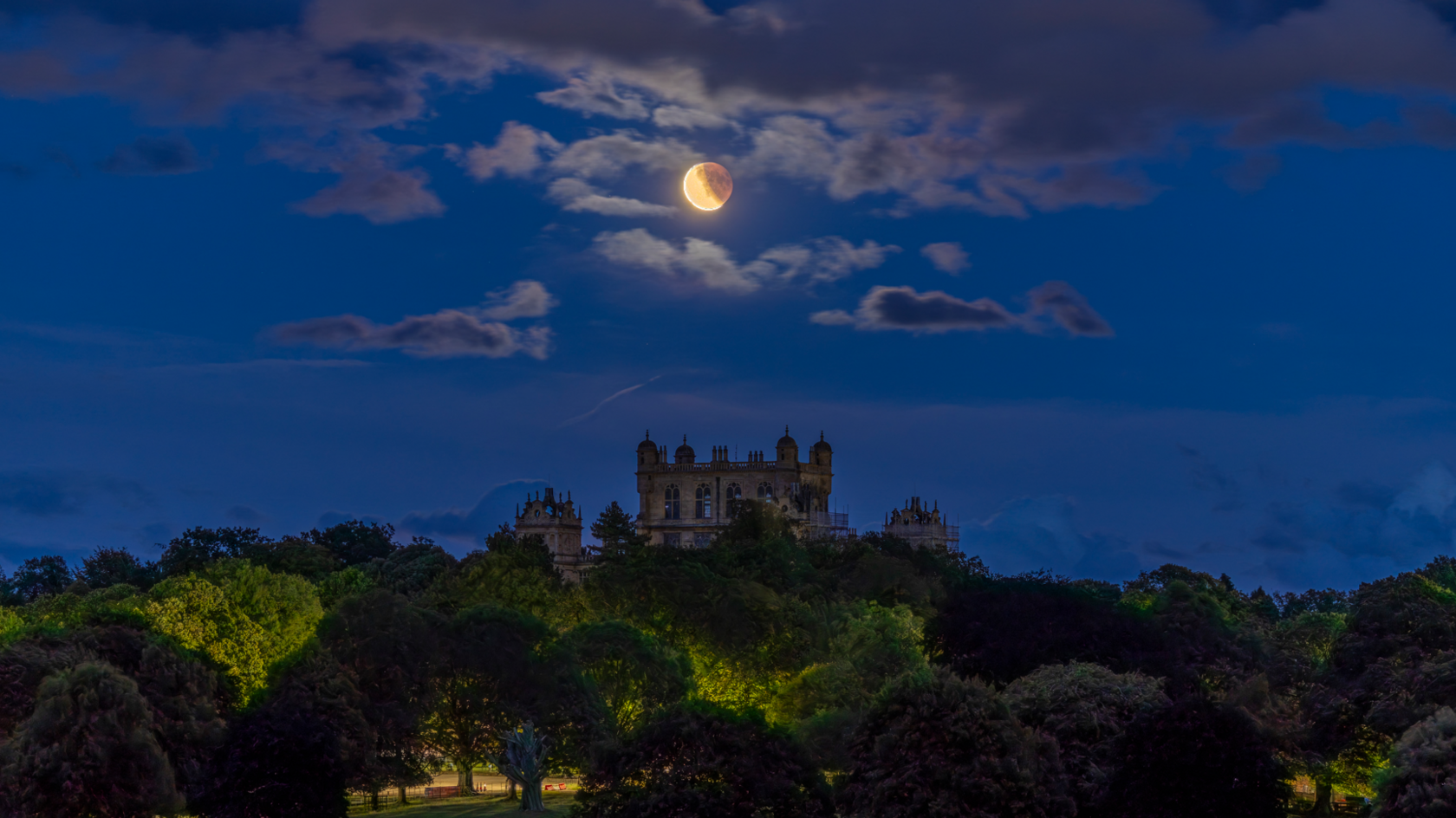 The blood moon above the top of Wollaton Hall which is poking up above the tree line.