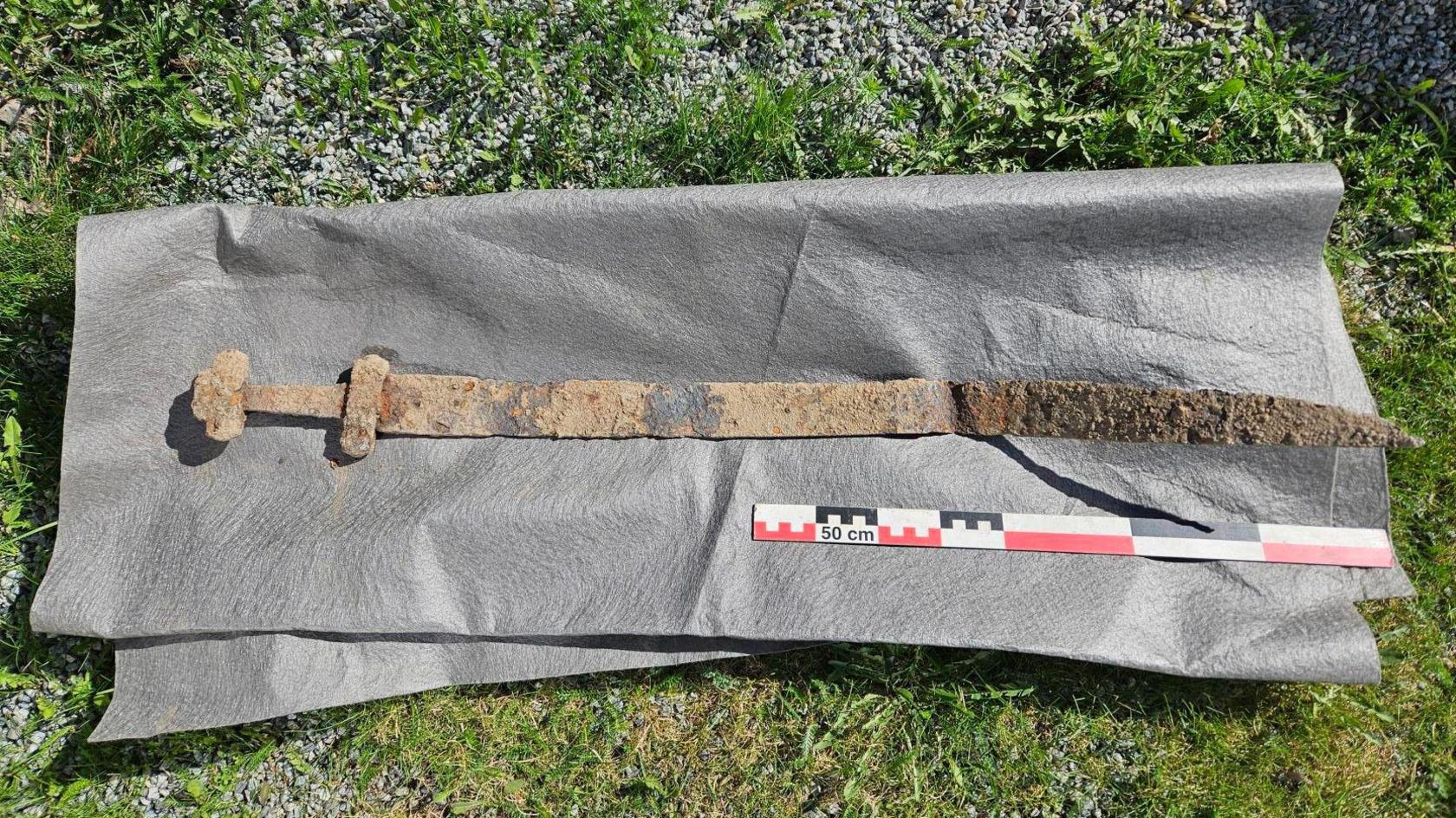 an ancient rusty viking sword laid out on a mat next to a ruler