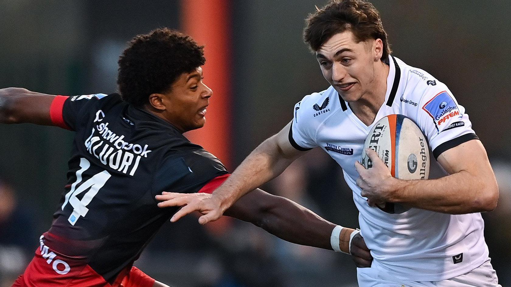 Noah Caluori, wearing a black Saracens shirt, tackles Campbell Ridl in a white Exeter shirt.