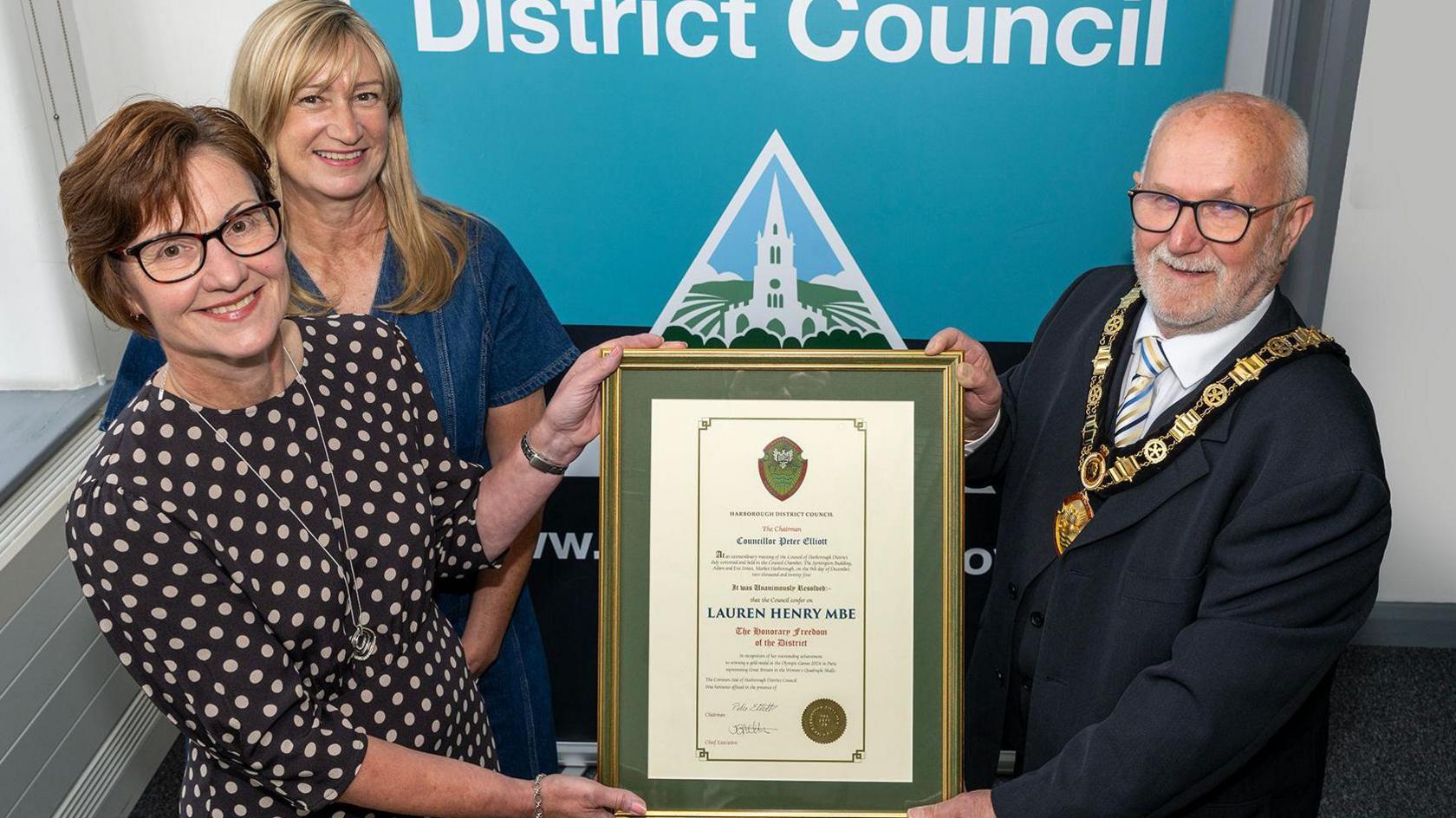 Lauren Henry's mother receiving the Freedom of the District honorary scroll from Peter Elliott, chairman of Harborough District Council, with Henry's aunt standing behind her mother