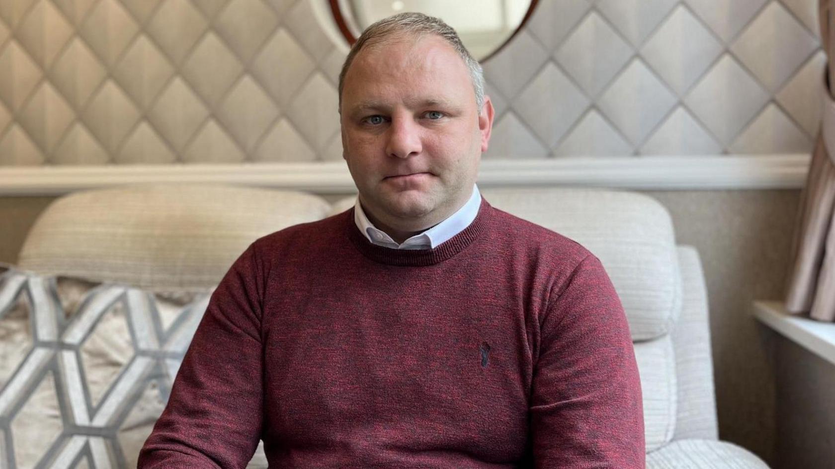 Gareth Jones yn eistedd ar soffa.