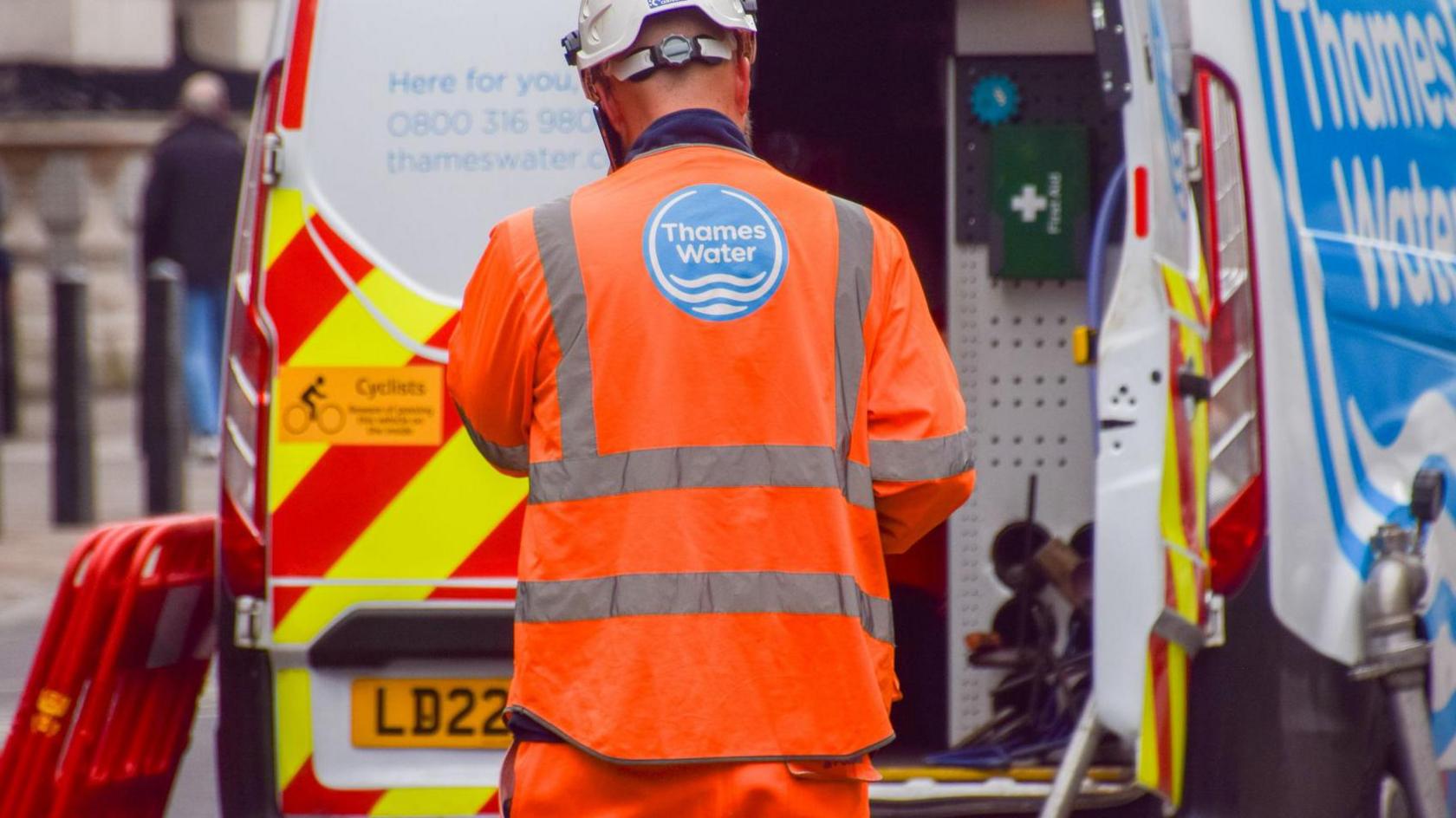 A Thames Water working wearing hi-viz clothing and a helmet, standing in front of a Thames Water van