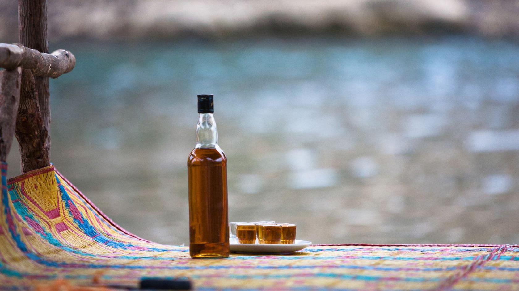 An alcohol bottle and shot glasses on at mat.