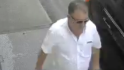 A man walking on a pavement wearing a white short sleeve shirt and sunglasses.
