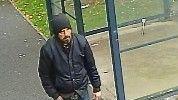 A CCTV image of William Riddell, walking past a bus stop wearing a black jacket, hat and blue jeans. He has a black beard. 