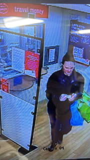 CCTV footage of Lisa Harper leaving a post office. She is carrying a number of plastic bags in one arm and is wearing a black tracksuit. She is standing near a plastic divider near the post office counter.