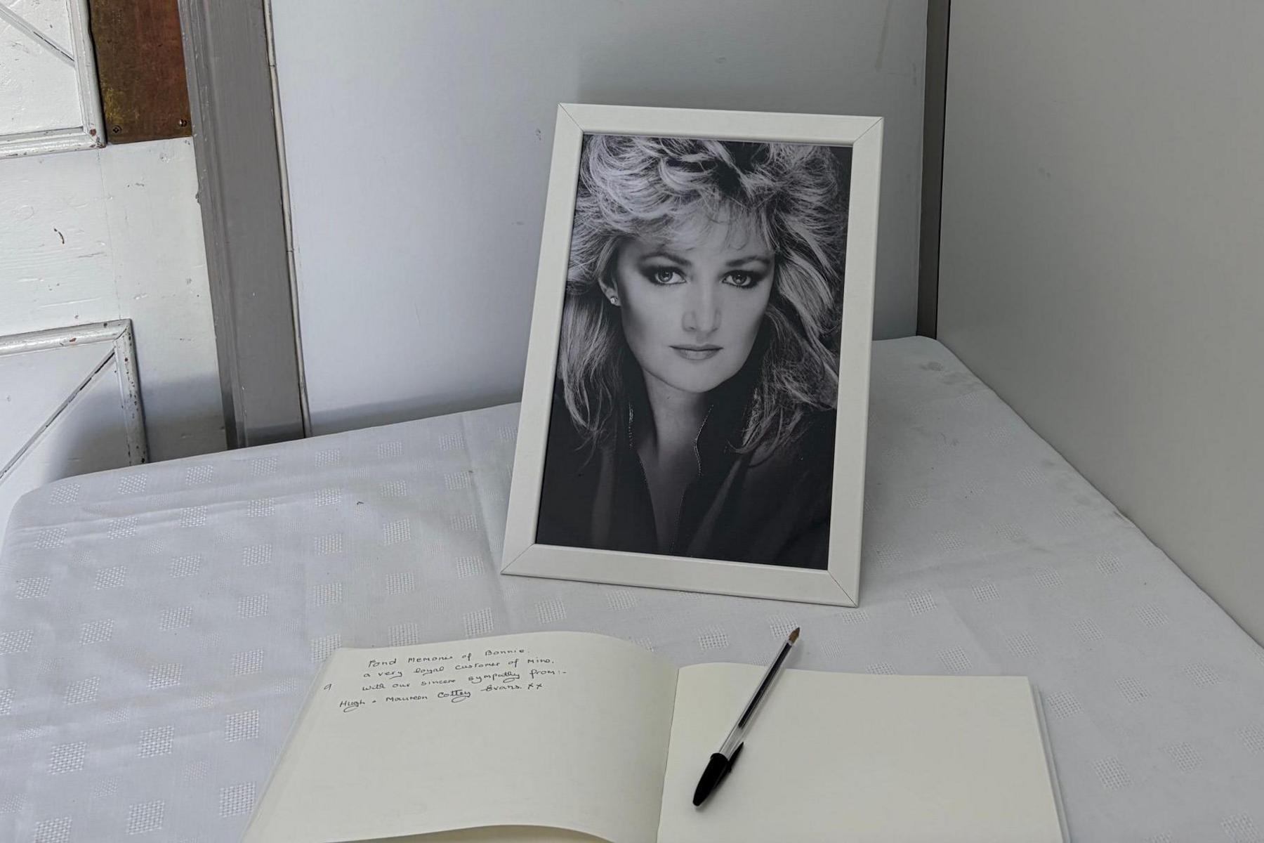 A black and white picture of Bonnie Tyler behind a book with a pen. A message can be seen written on the left hand page.