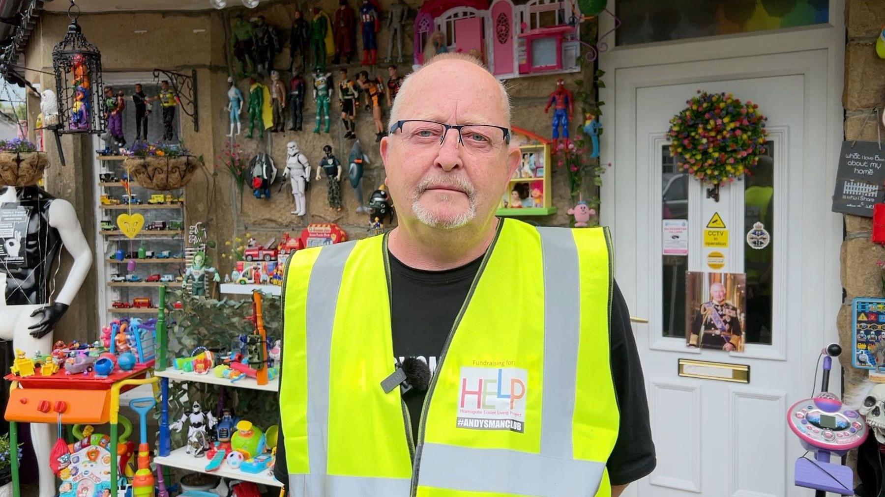 Paul Ivison dressed in a hi-vis jacket in front of his toy garden in the background