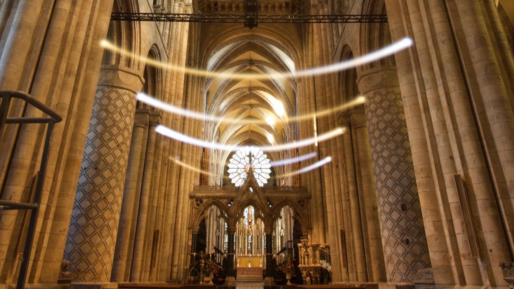 Chorus consists of eight huge pendulums suspended in the vaulted ceiling of Durham Cathedral. They are swinging and creating arcs shining in yellow, orange and white.