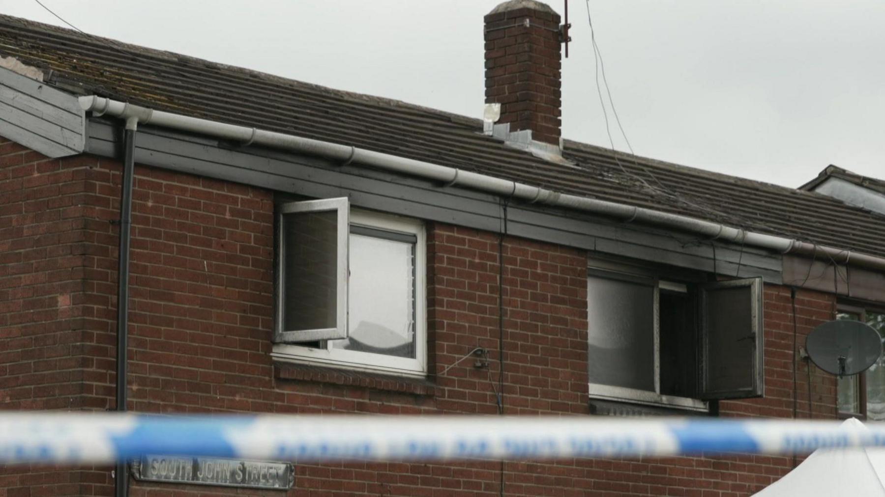 Burnt out window frames with police tape in the foreground at the crime scene.