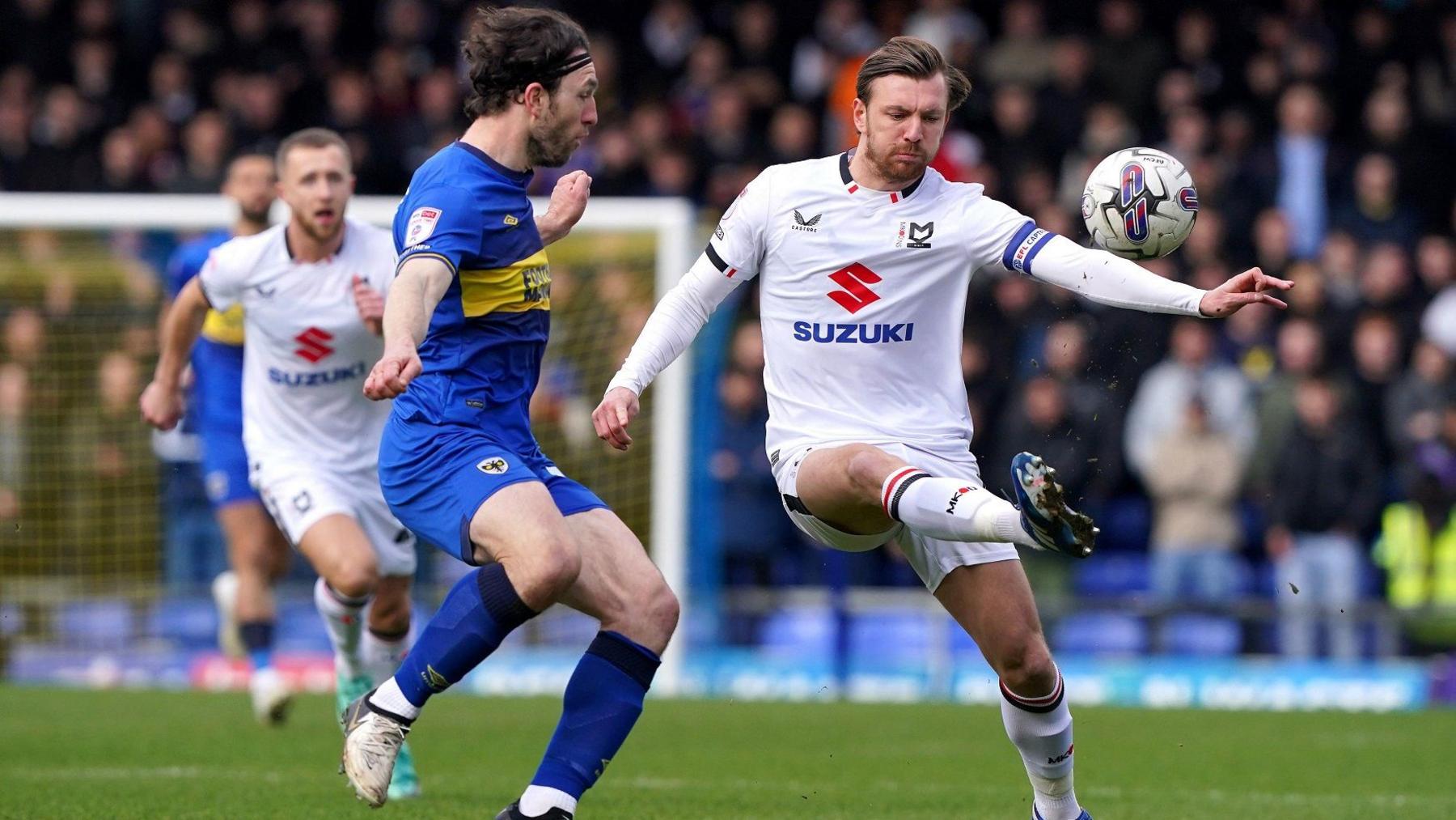 Footballers from AFC Wimbledon (in blue) and MK Dons (white kit kicking the ball