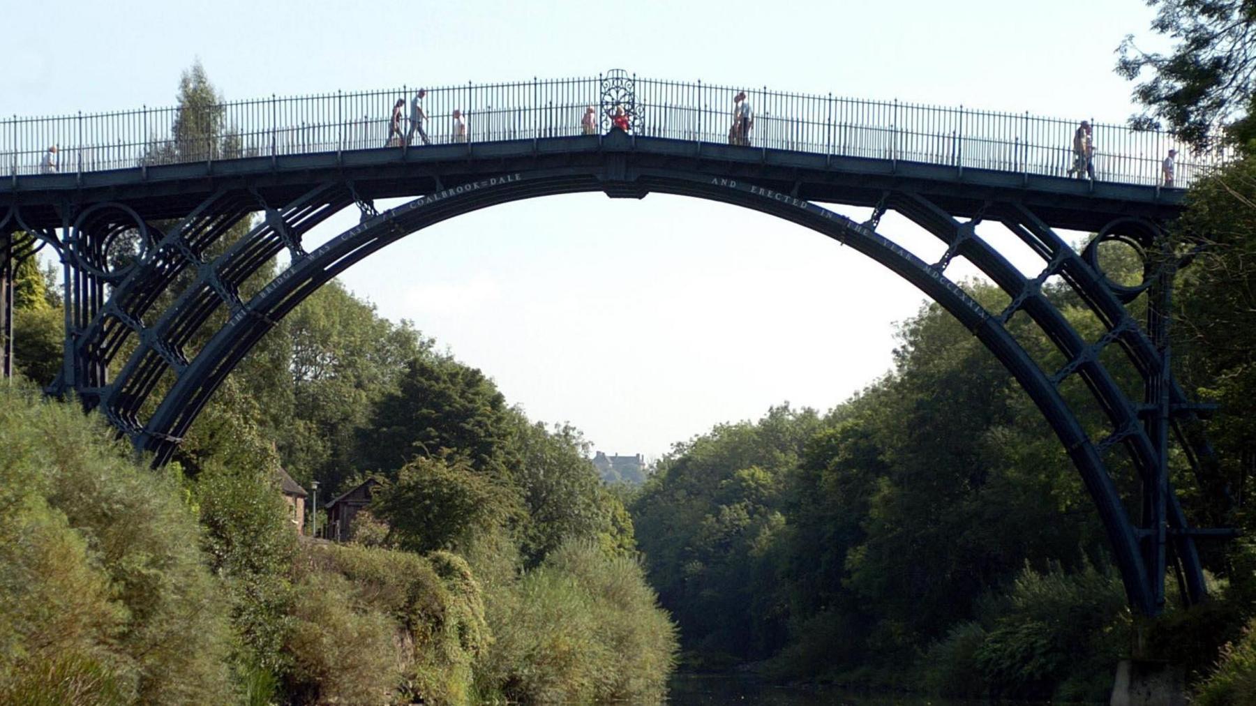 Image shows Shropshire's Ironbridge gorge, a huge black iron bridge over the river with thick green trees either side.