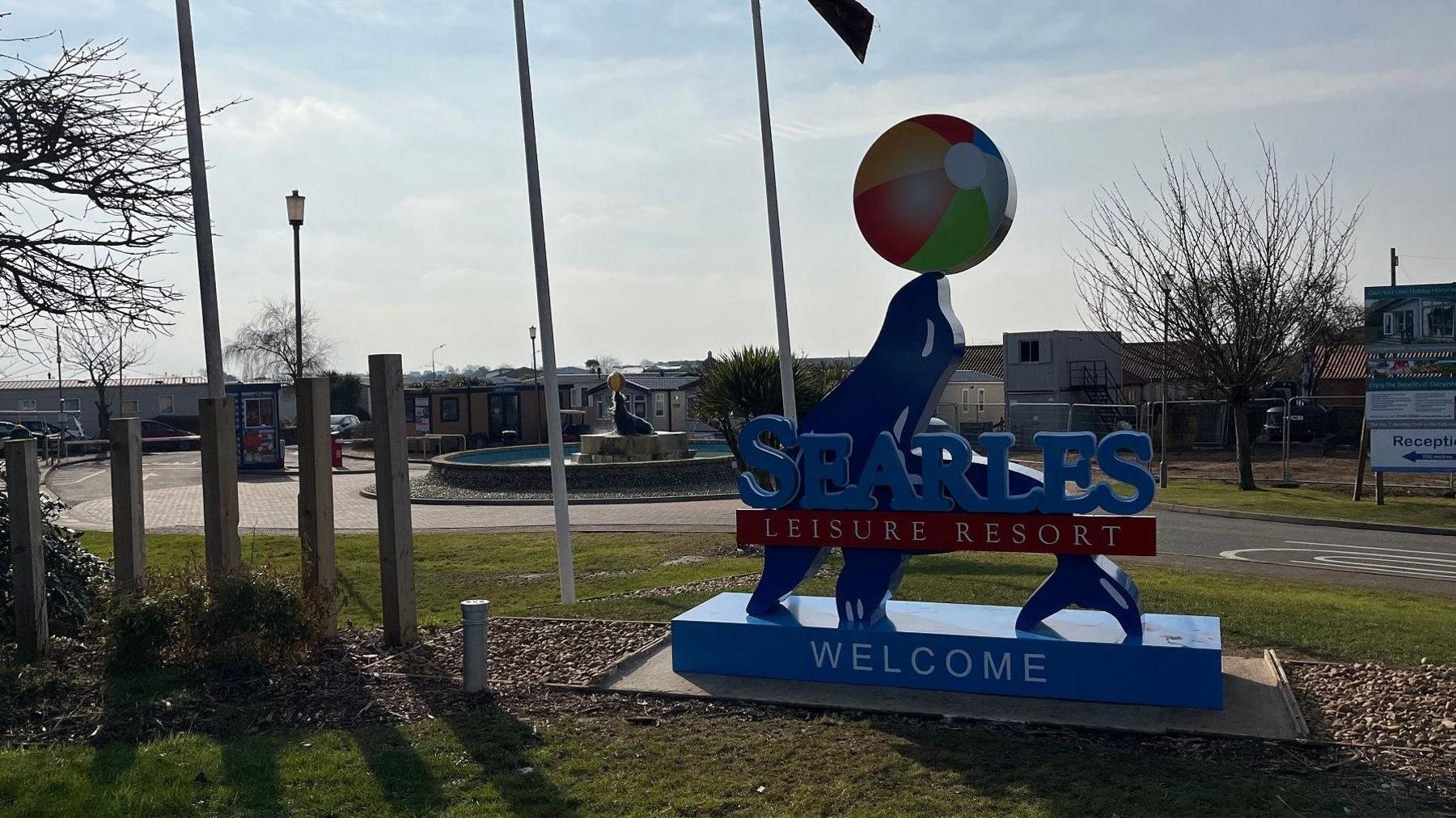 Exterior view of Searles holiday park. A blue sign in the shape of a seal says it welcomes visitors to Searles Leisure Resort. 