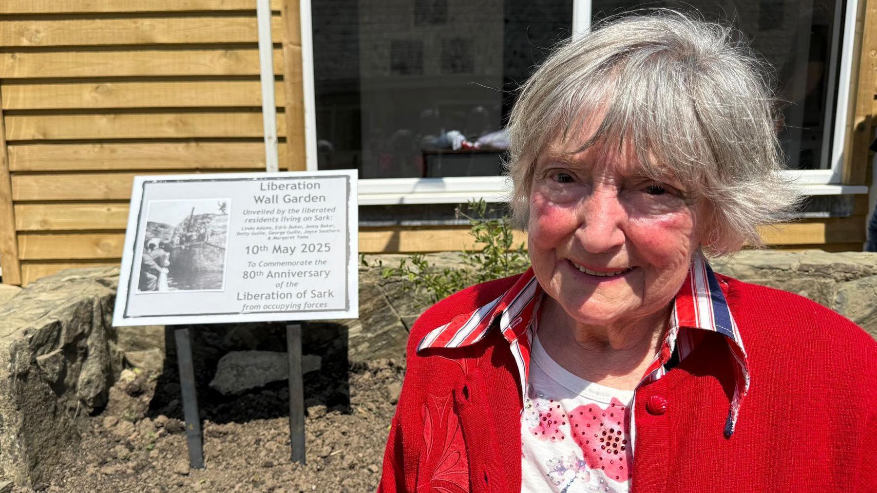 Maisie Le Page is smiling as she stands next to the plaque which reads: LIBERATION WALLED GARDEN - UNVEILED BY THE LIBERATED RESIDENTS LIVING ON SARK 10 MAY 2025.