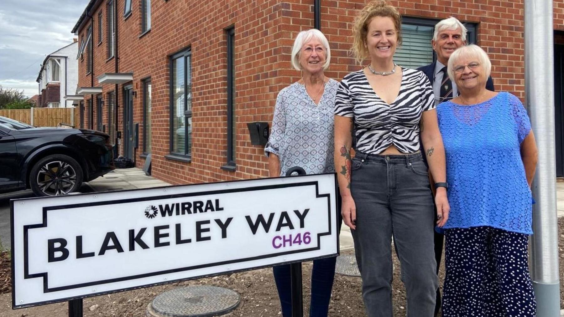 A white sign with black writing which says Blakeley Way CH46. It has the Wirral Council logo. Sandra Blakeley, Stephanie Miller, Tony Blakeley, Val Frost are pictured alongside the sign.