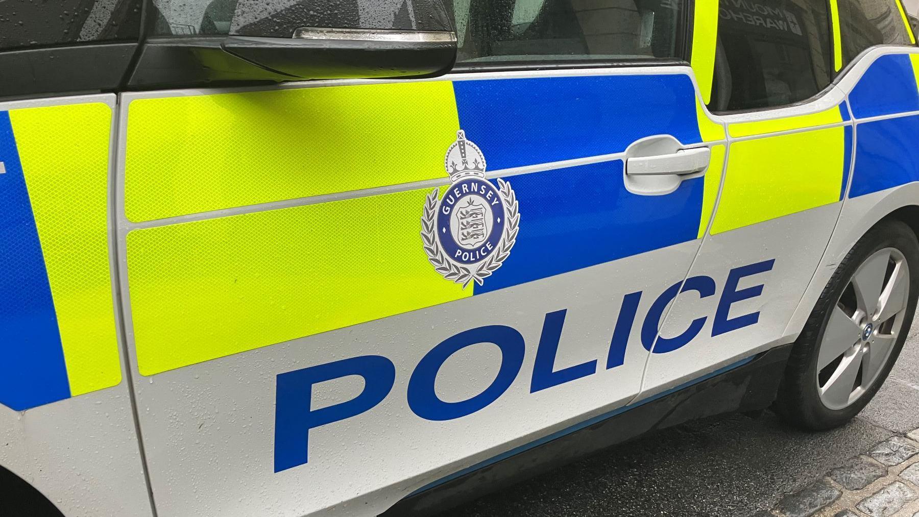 The door of a Guernsey Police car, with the words Guernsey Police on and yellow and blue reflective boxes.