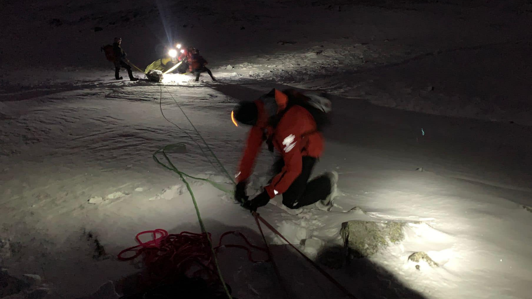 Patterdale Mountain Rescue Team assembling a rope system during a rescue. There is a team member wearing red in the foreground and other team members wearing head torches a few metres away.