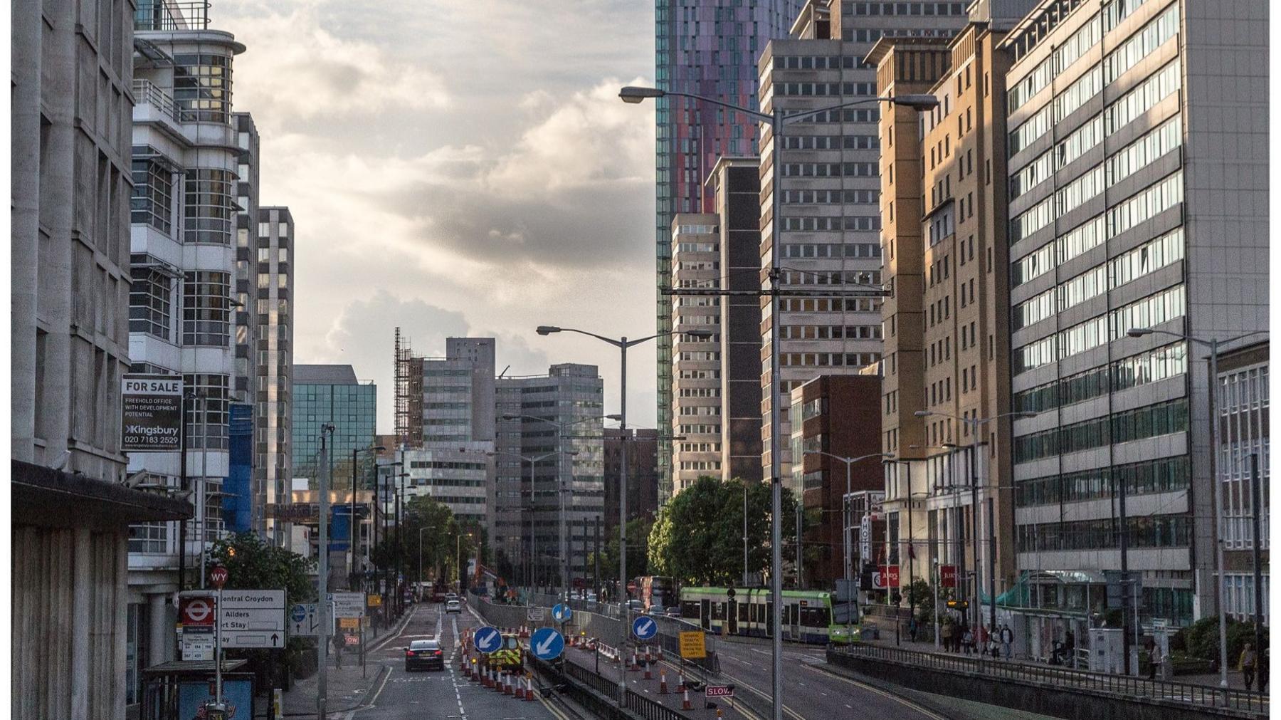 A picture of the Croydon skyline - roadworks can be seen in the foreground, while tall, glass-fronted buildings are lit by the morning sun.  