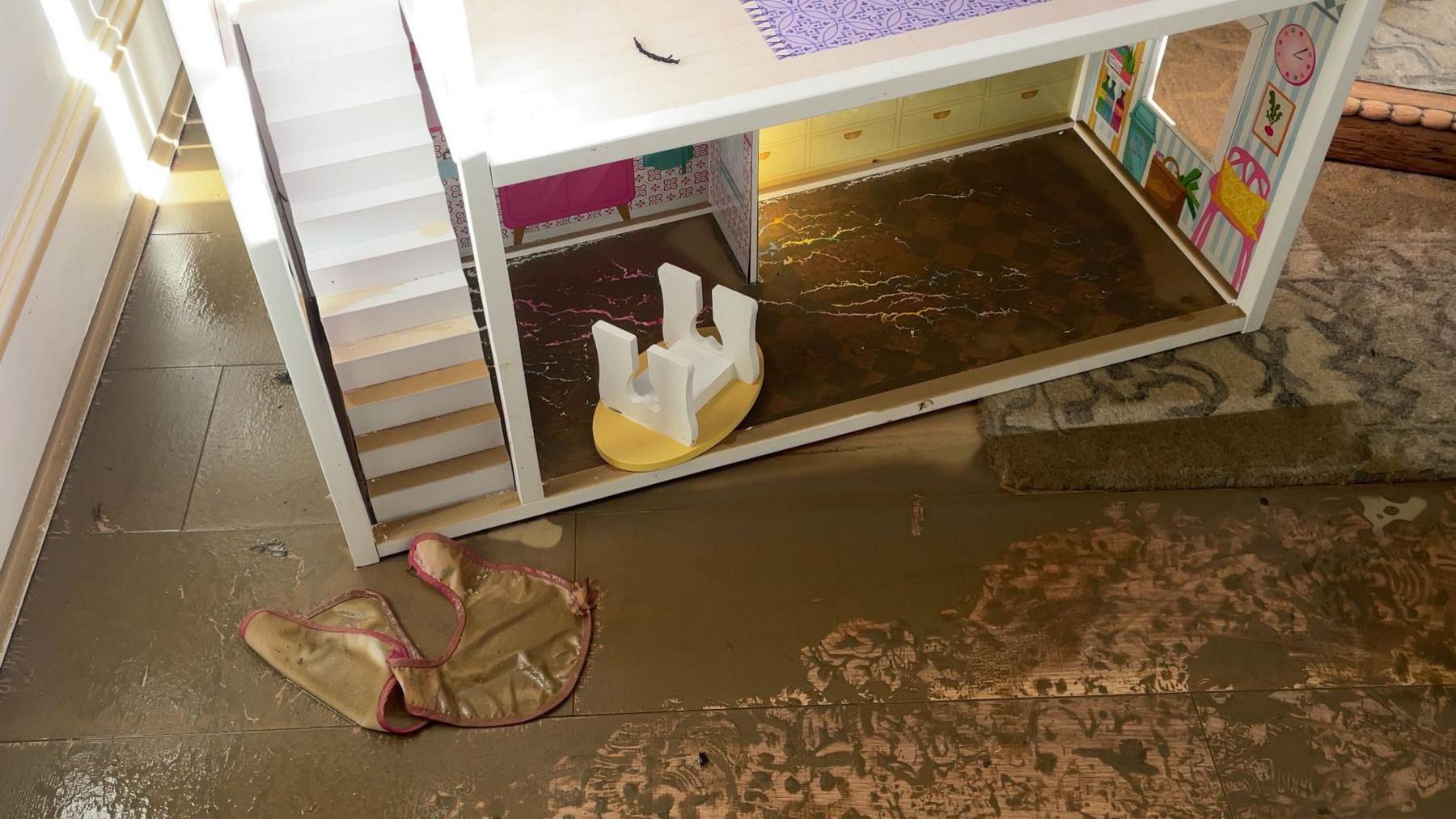 Shot of a white-coloured doll's house on a tiled floor covered in mud left by the floodwater. 